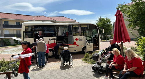 Reisebus von Deutschen Roten Kreuz steht vor Seniorenzentrum. Senioren steigen ein.