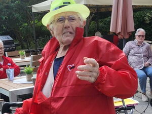 Senior in roter Kleidung und gelben Hut am Rollator.