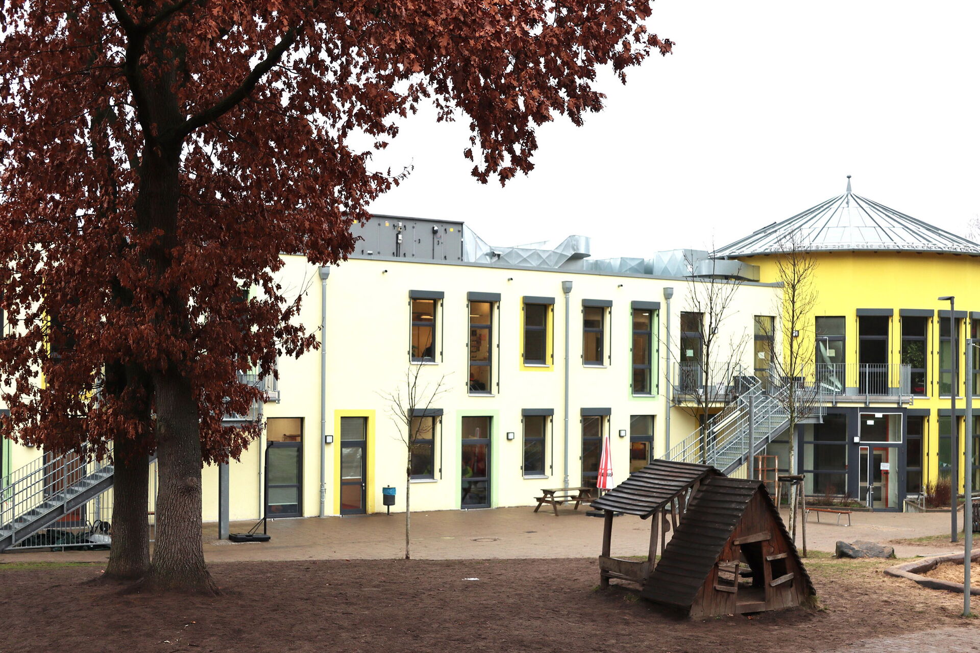Gebäude von außen, zwei Geschosse. Schule und Hort. Außentreppen führen zum zweiten Stockwerk, Fassade ist gelb.