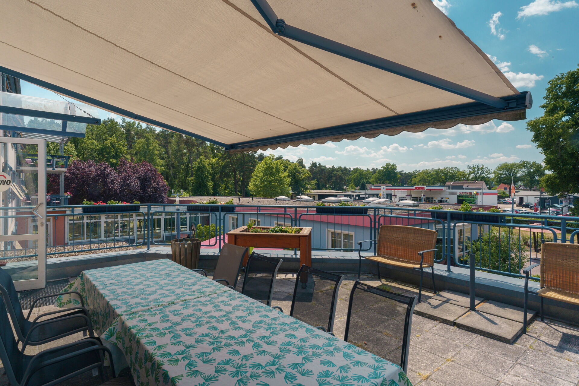 Terrasse mit Markise, darauf ein langer Tisch mit Stühlen.