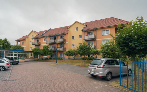 Parkplatz, parkende Autos, ein orangenes Wohngebäude mit Balkonen.