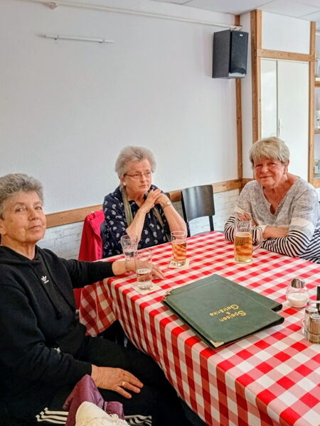 3 Frauen sitzen am Tisch. Speisekarten und Getränke vor ihnen.