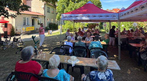 Menschen sitzen draußen im Schatten unter Bäumen und roten Pavillons.
