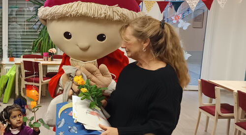 Der Sandmann in Lebensgröße nimmt Karten, Bilder und Blumen zum Geburtstag entgegen. Frau übergibt ihm alles. Kinder stehen um ihn rum.