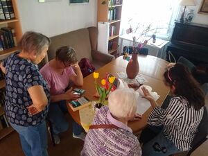 Drinnen. Tisch, Sofa, vier Frauen. Auf dem Tisch ein Osterstraus an dem bunte Ostereierhängen.