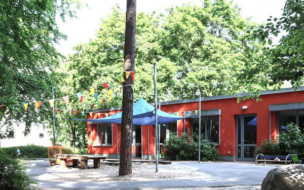 Spielplatz vor rotem flachen Kita Gebäude.