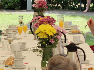 Draußen, Festzelt, mit rot-weißen Wimpel, roten und weißen Luftballons geschmückt. Lange Festtafel an der Senioren mit Kaffee und Kuchen sitzen, Das Wetter ist sonnig.