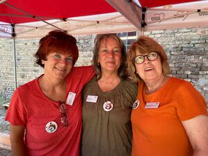 Portrait. 3 Frauen engbeieinander. Sie stehen unter einem roten AWO Pavillon. 1. Frau: rote Haare, Sonnenbrille auf den Kopfgeschoben, rotes Kleid. 2. längere braun-graue Haare, und ein olivefarbenes Oberteil. 3. volle braune Haare, orangenes T-Shirt.