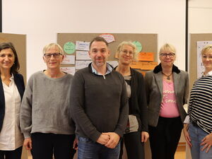 Gruppenfoto: 6 Personen vor Pinnwänden. Ein Mann im dunkelgrauen Pullover steht in der Mitte.