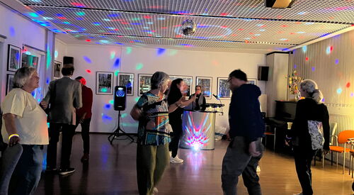 wenige Menschen tanzen unter Discokugel und buntem Licht.