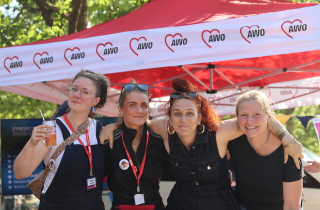 4 Frauen, gut gelaunt, Arme umeinander gelegt lächeln in die Kamera.