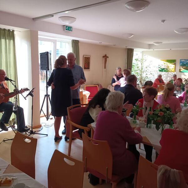 Raum mit Kaffeetafeln, Mann mit Gitarre und zwei tanzende Paare.