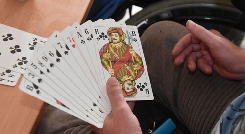 Rommé Spiel, Eine Person hält aufgefächert Karten in der Hand. Auf dem Tisch liegen Kreutz 7, 8, 9