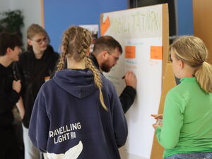 Mann schreibt an großes Flipchart. Kleingruppe steht drum herum.