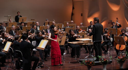 Hier sehen sie ein Orchester mit einer Frau im roten Kleid mit einer Geige