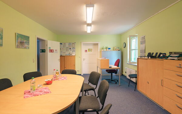 Besprechungsraum. Ovaler Tisch mit 6 Stühlen, rechts an der Wand steht ein Schrank.