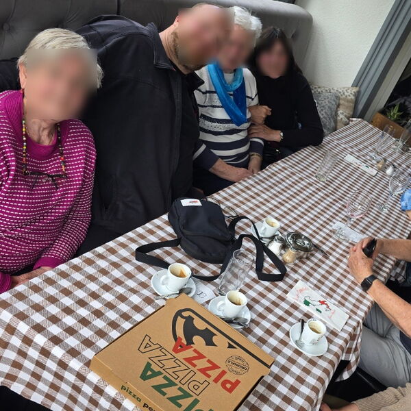 8 Personen an einen Tisch. Auf dem Tisch ein Pizzakarton und Tassen und Gläser.