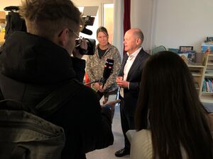 Scholz im Interview. Kamera ist auf ihn gerichtet. Vor ihm ein Mikrofon. Frau steht neben ihm.