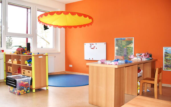 Spielzimmer. Freundlich eingerichteter Raum für Kinder. Die Wand ist orange, Regal mit Lego und Spielzeug links am Fenster.