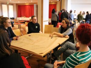 Fünf Menschen sitzen um einen Tisch. Auf dem Tisch ein Flipchartpapier mit Notizen in verschiedenen Farben.