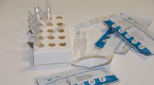 Drei verpackte Corona Tests. Ampullen in einem Pappständer