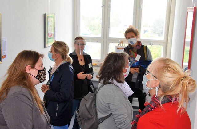 Frauen in einem Raum mit Bildern an der Wand. Frauen tragen OP- Und Stoffmasken