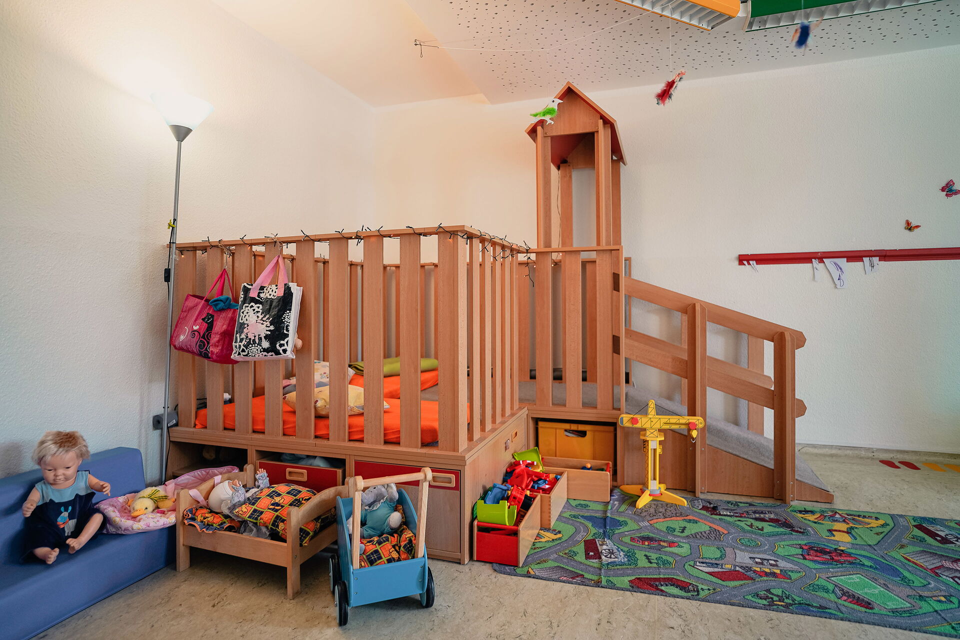 Spielzimmer. Mit Puppen, Puppenwagen, Puppenbett, ein Kinder-Straßen-Teppich und ein Kindergarten-Hochebene mit Matratzen und Kissen.