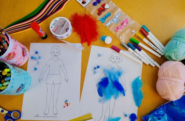 Tisch von oben mit Mal- und Bastelutensilien. Zwei Bilder nebeneinander, Junge und Mädchen. Auf dem Bild des Mädchens sind blaue Federn geklebt. Stifte, Schere, Wollknäuel, blaue Perlen, Prittstift