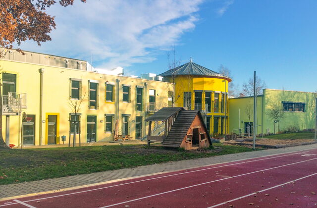 Großes gelbes Schulgebäude. Laufbahn für Sport, draußen auf dem Schulhof.