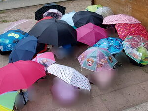 Kinder hocken auf dem Boden und haben viele bunte Regenschirme über sich aufgespannt.