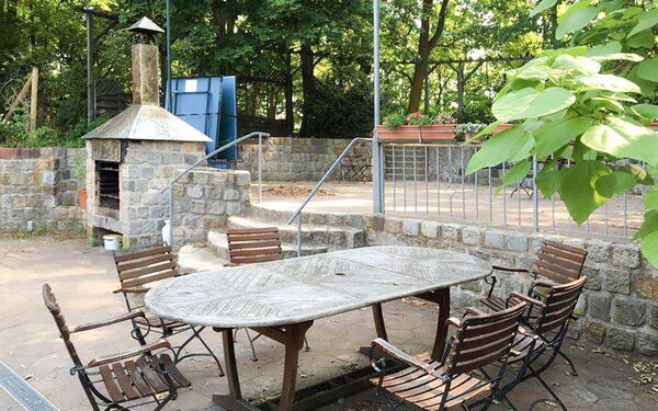 Draußen. Terrasse. Langer Holztisch mit 6 Stühlen. Weiter hinten kleiner Pizze / Brot Backofen aus Stein.