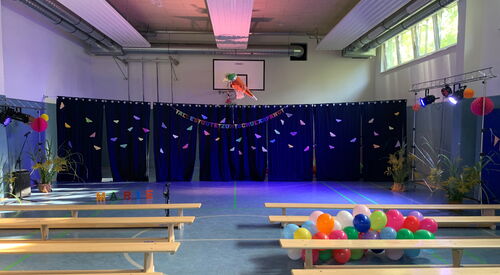 Bunt geschmückte Turnhalle mit vielen Ballons rechts zwischen Turnbänken.
