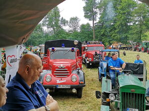 Menschen im Traktoranhänger. Dahinter fahren Traktoren und alte Feuerwehrautos.