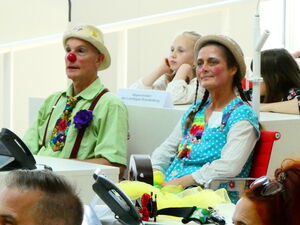 2 Klinikclowns, Kinder und Erwachsene sitzen im Plenarsaal.