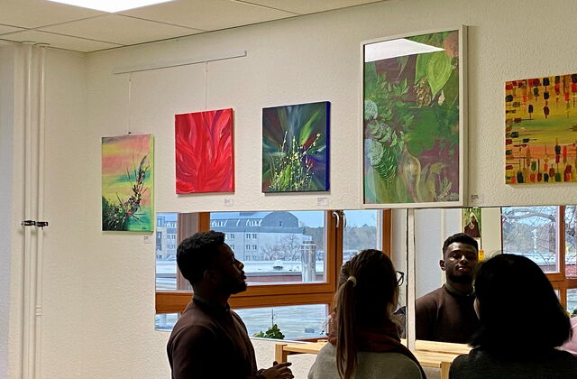 5 Bilder an einer Wand. 3 Besucher schauen sich die Bilder an.