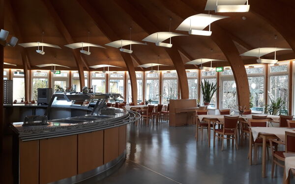 Großer Speisesaal Halb Runde Theke. Tische mit Stühlen stehen rechts an den Fenstern.