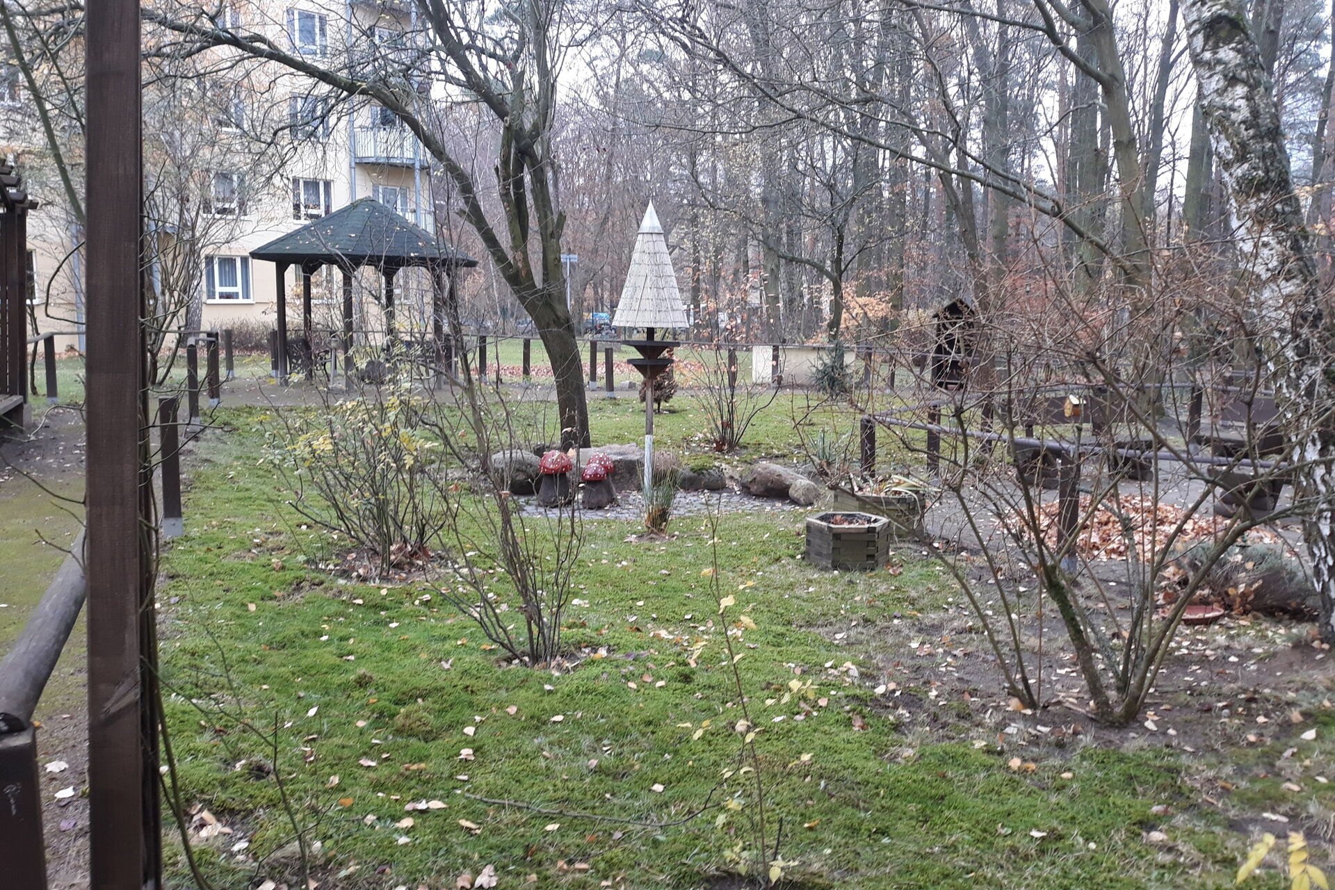 Kleine Parkanlage. Kahle Bäume und Sträucher, weiter hinten ein kleiner fester Pavillon aus Holz.
