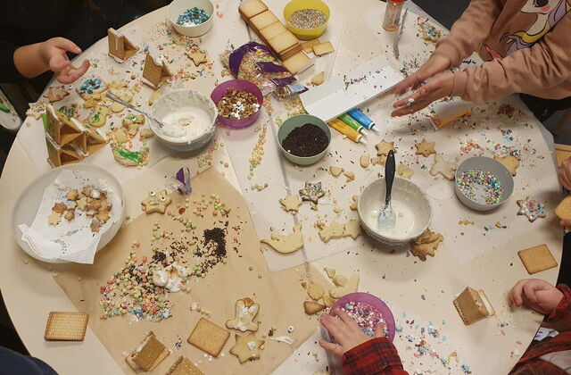 Weihnachtsplätzchen dekorieren. Runder Tisch von oben. Plätzchen, Glasuren, bunte Streusel. Kinderhände die mit dekorieren beschäftigt sind.