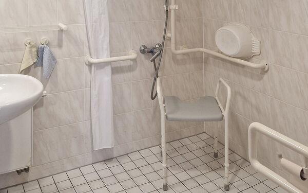 Barrierefreies Badezimmer mit Ebenerdiger Dusche, Duschhocker und Haltegriffe an den Wänden.
