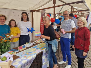 Der AWO Vorstand an einem Stand. Eine Frau im Stand hat einen blauen Luftballonhund in der Hand, ein mädchen und noch eine Frau stehen neben ihr.