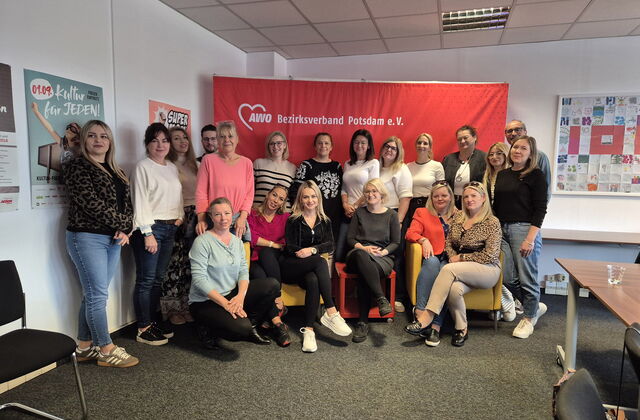 Gruppenbild: In einem Konferenzraum vor einer roten AWO Stoffwand stehen und sitzen 20 Menschen.
