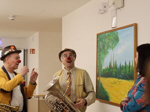 Zwei Klinikclowns auf dem Flur machen Seifenblasen für die Ministerin. Die Clowns haben auch Blasinstrumente bei sich.