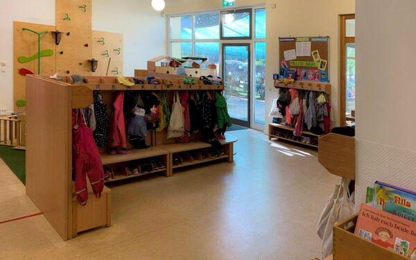 Mehre Garderoben, da hängen Jacken und Beutel und in einem Fach darunter stehen die Schuhe der Kinder.