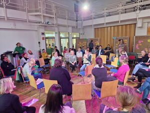 Großer Raum, Gesprächsrunde Menschen sitzen in Stuhlkreisen. Hinten im Raum sind 4 Flipcharts an denen farbige Moderationskarten angepinnt sind.