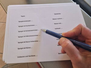 Bestellzettel mit den Gerichten und Getränken. Hand mit Kugelschreiber.