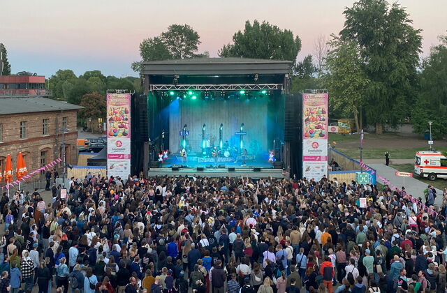 Eine große Bühne, rechts und links davon Banner vom Akzeptanzfestival. Vor der Bühne viele feiernde Menschen. Auf der Bühne eine Band.