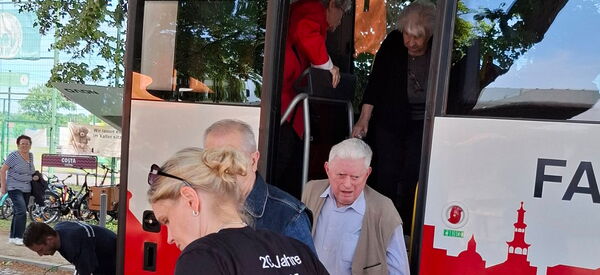 Reisebus mit hohen Stufen. Mitarbeiterin hilft Senioren beim Aussteigen.