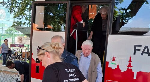 Reisebus mit hohen Stufen. Mitarbeiterin hilft Senioren beim Aussteigen.