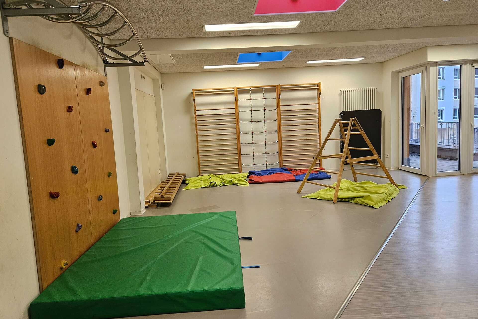 Raum mit Kletterelementen. Boulderwand links, Sprossenwand in hintere Bereich des Raums.