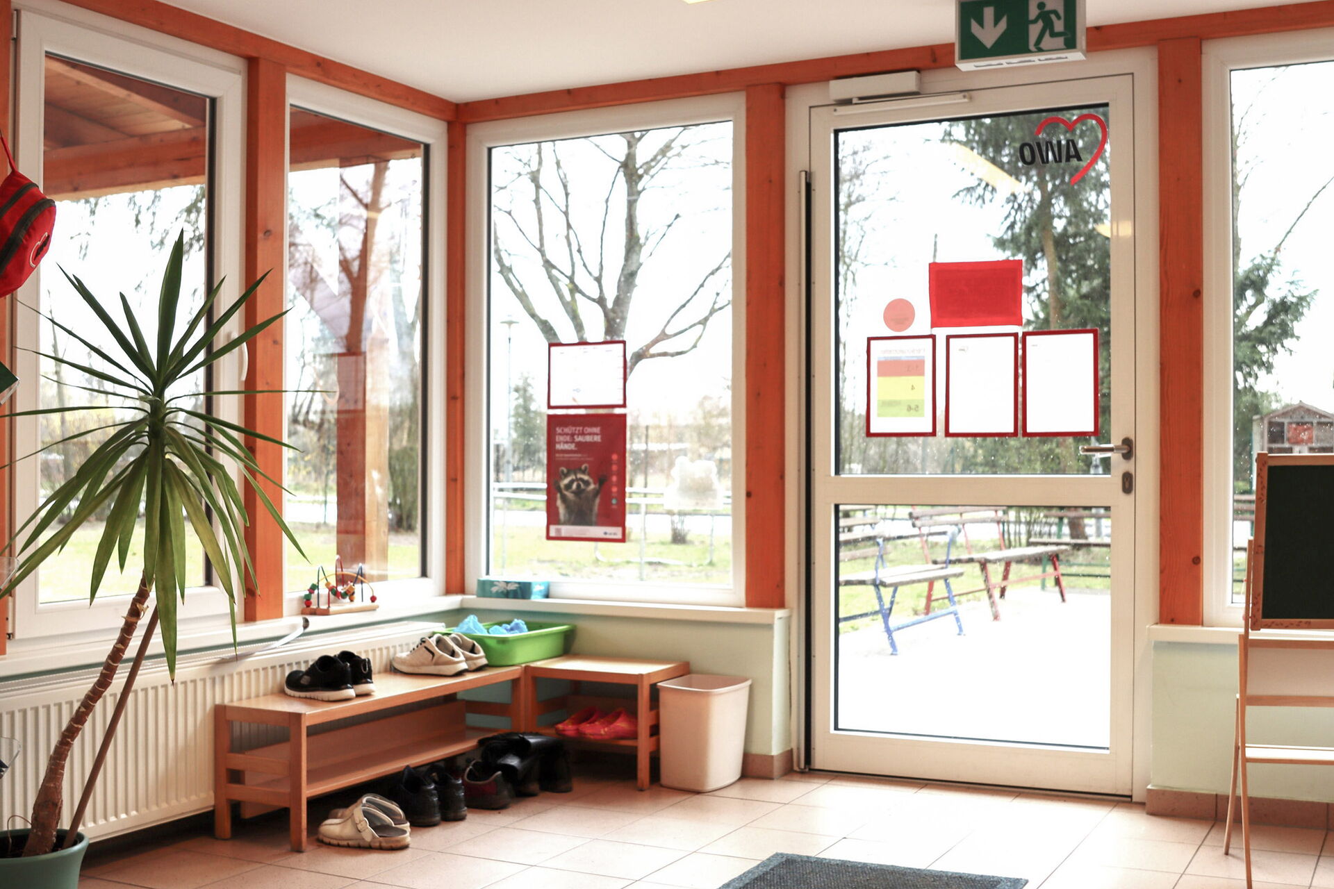 Verglaster Eingangsbereich mit kleinem Schuhregal in er Ecke. Blick nach draußen.
